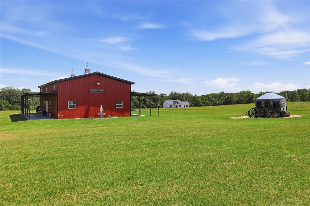A red barn with a covered porch stands in a large, grassy field — 18605 NW COUNTY ROAD 235A, ALACHUA, FL