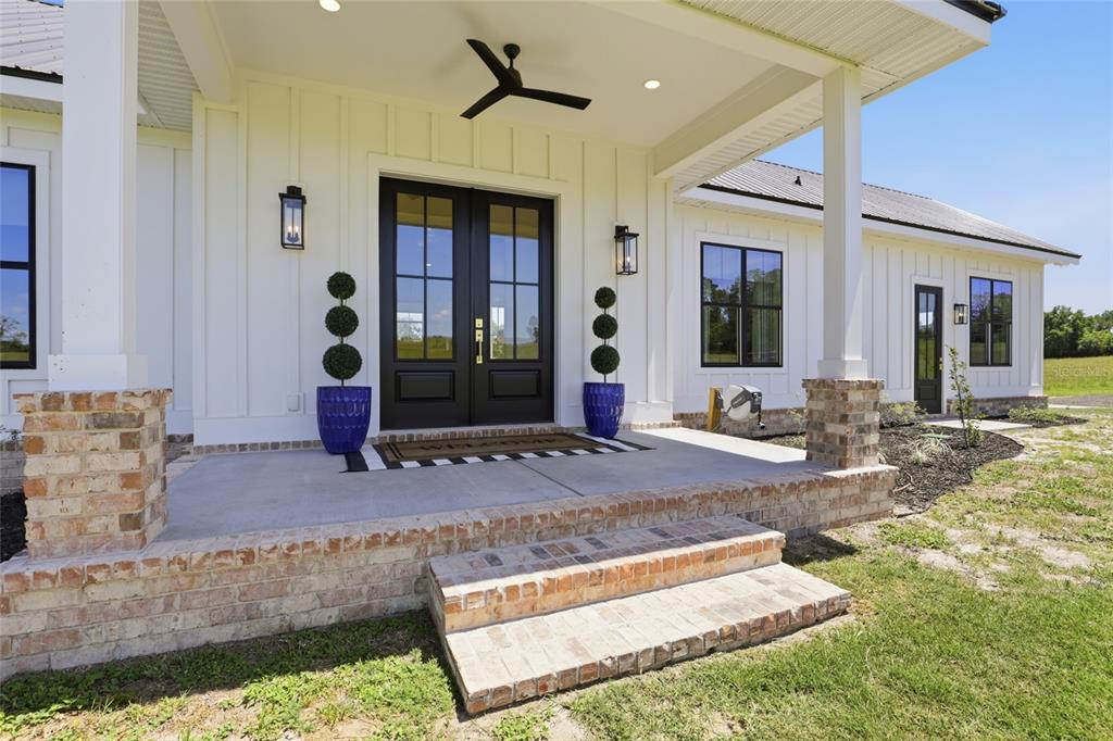 A white farmhouse exterior features a brick porch, double front doors, and black window frames — 18605 NW COUNTY ROAD 235A, ALACHUA, FL
