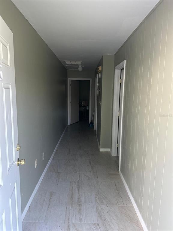 A narrow hallway with light-colored tile flooring leads to a doorway at the far end — 214 N CHESTNUT ROAD, LAKELAND, FL
