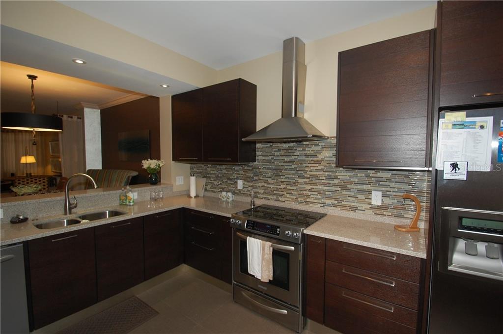 A modern kitchen features dark wood cabinets, stainless steel appliances, and a mosaic tile backsplash — 4634 MIRADA WAY UNIT 19, SARASOTA, FL