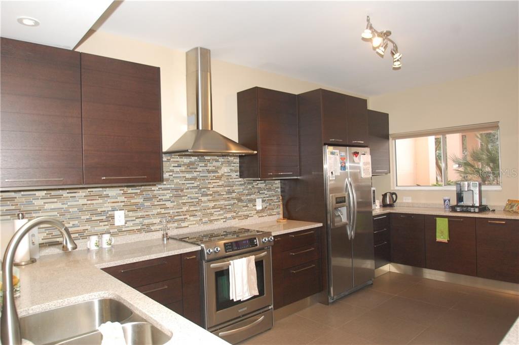 A modern kitchen features dark wood cabinets, stainless steel appliances, and a tiled backsplash — 4634 MIRADA WAY UNIT 19, SARASOTA, FL