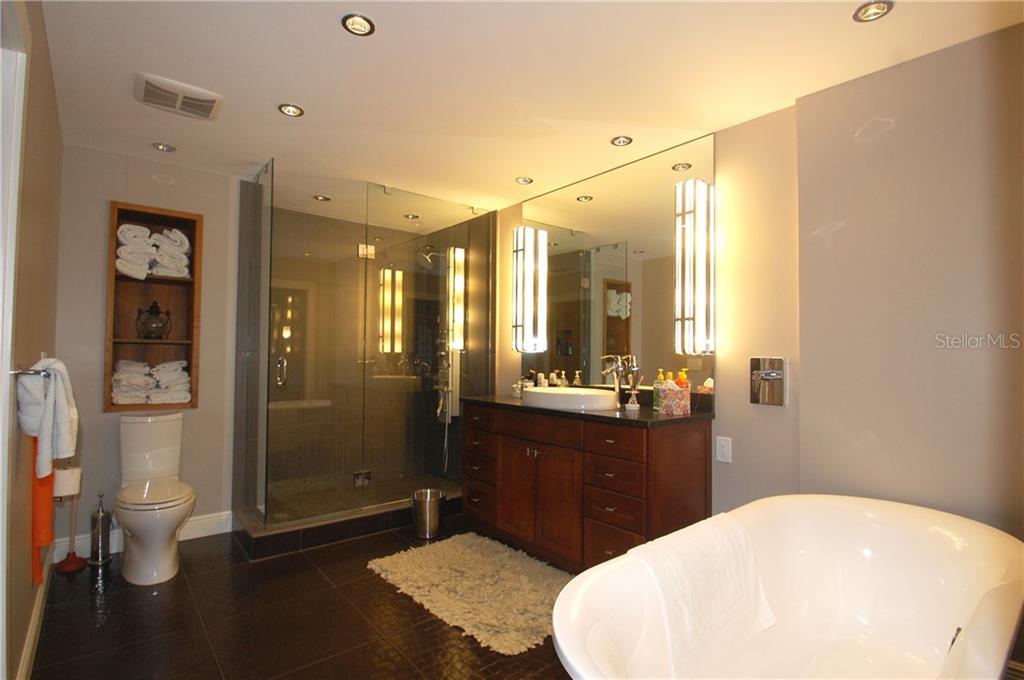A modern bathroom features a glass-enclosed shower, a dark wood vanity, and a freestanding soaking tub — 4634 MIRADA WAY UNIT 19, SARASOTA, FL