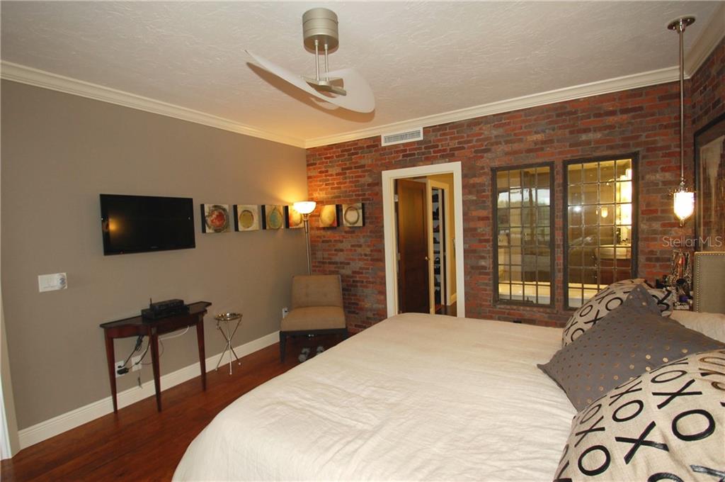 A bedroom features a brick accent wall, a ceiling fan, and a flat-screen television — 4634 MIRADA WAY UNIT 19, SARASOTA, FL