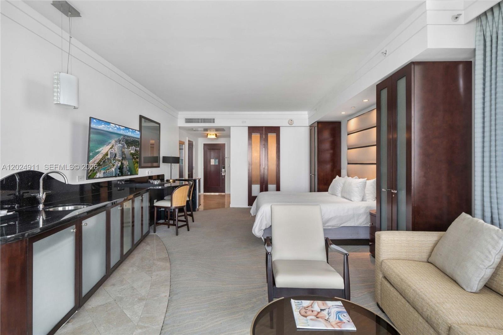 A hotel room features a kitchenette, a bed, a seating area, and dark wood cabinetry — 4391 Collins Ave # 1002, Miami Beach FL 33140, MIAMI BEACH, FL