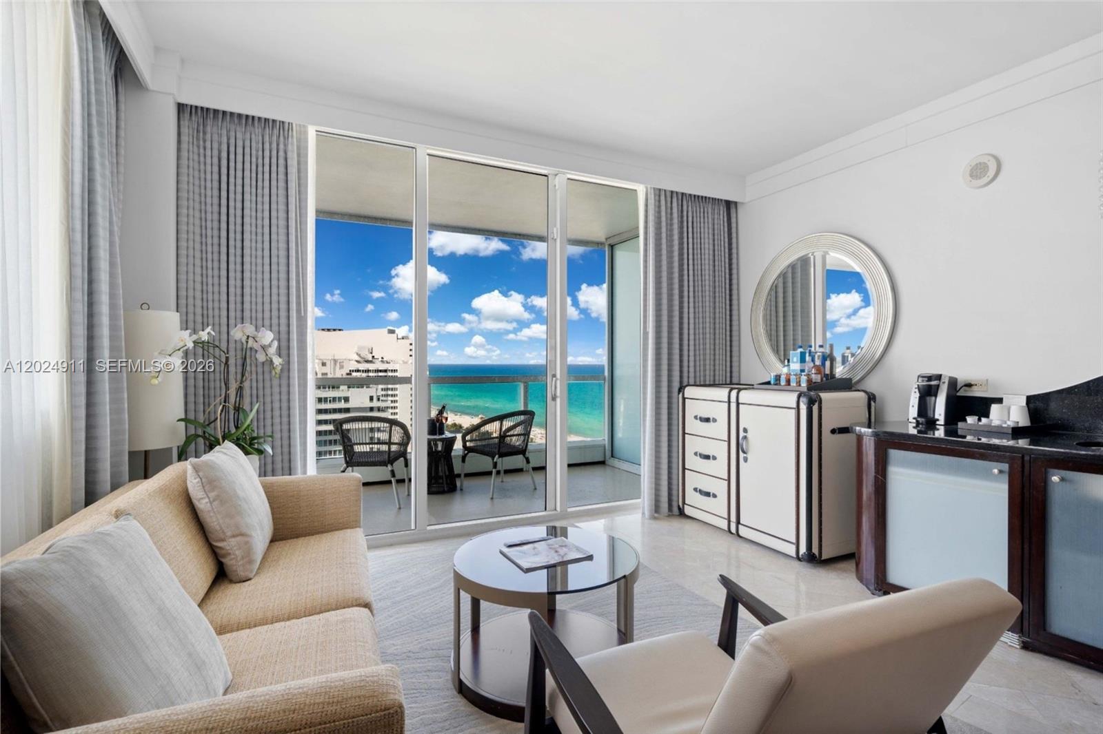A living room features a beige sofa, glass coffee table, and a balcony overlooking the ocean — 4391 Collins Ave # 1002, Miami Beach FL 33140, MIAMI BEACH, FL