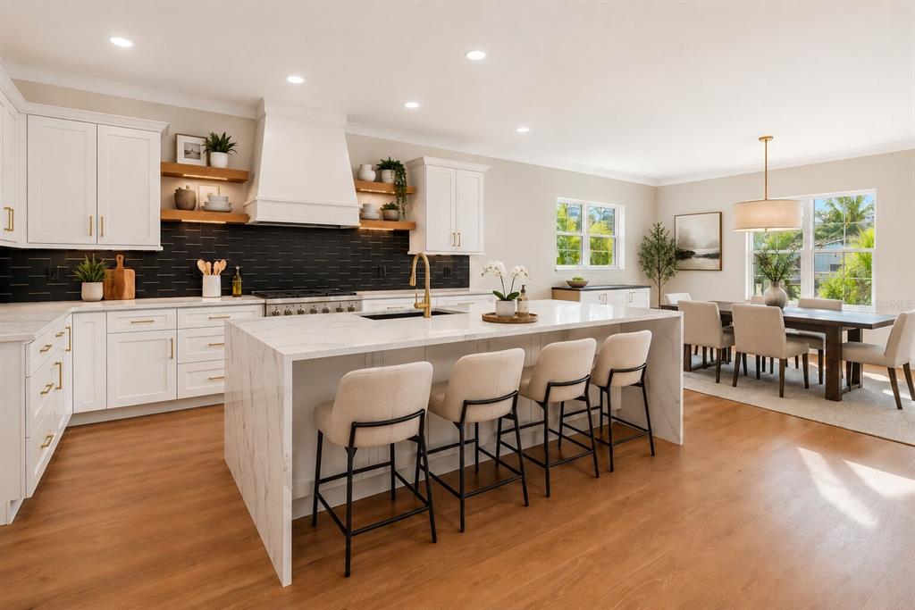 A modern kitchen features white cabinetry, a marble-topped island with four stools, and wood flooring — 4314 W VASCONIA STREET, TAMPA, FL