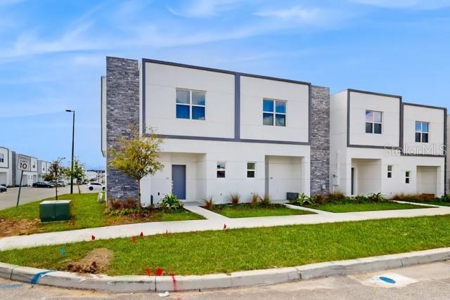 A modern two-story townhouse exterior with white walls, stone accents, and a front lawn — 213 FAMAGUSTA DRIVE, DAVENPORT, FL
