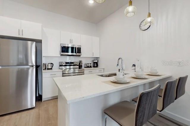 A modern kitchen features white cabinetry, stainless steel appliances, and a quartz-topped island with seating — 213 FAMAGUSTA DRIVE, DAVENPORT, FL