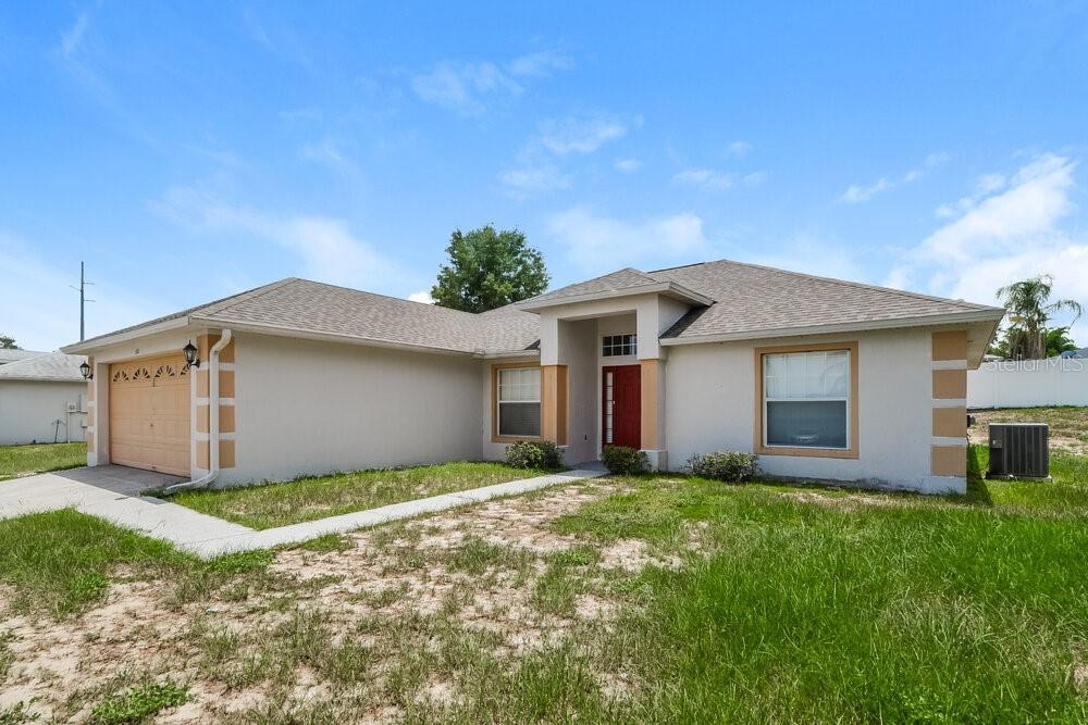 A single-story house with a tan exterior, a red front door, and a two-car garage — 310 COUNTRY LAKES CIRCLE, GROVELAND, FL