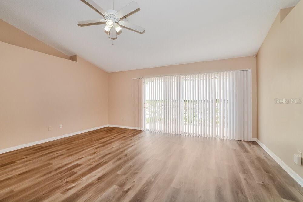 An empty room features light-colored walls, wood-look flooring, a ceiling fan, and vertical sliding blinds — 310 COUNTRY LAKES CIRCLE, GROVELAND, FL