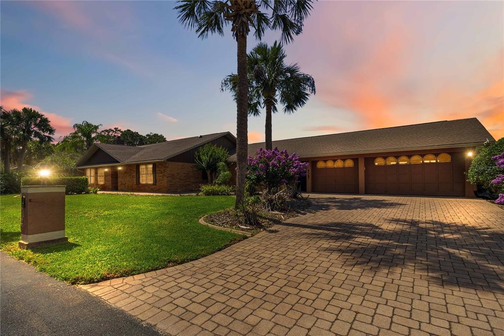 A single-story brick house with a paved driveway and palm trees at sunset — 5367 CROOKED OAK CIRCLE, ST CLOUD, FL