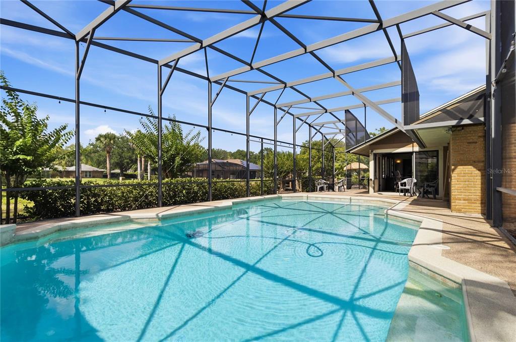 A swimming pool sits inside a screened-in lanai with a brick exterior wall — 5367 CROOKED OAK CIRCLE, ST CLOUD, FL