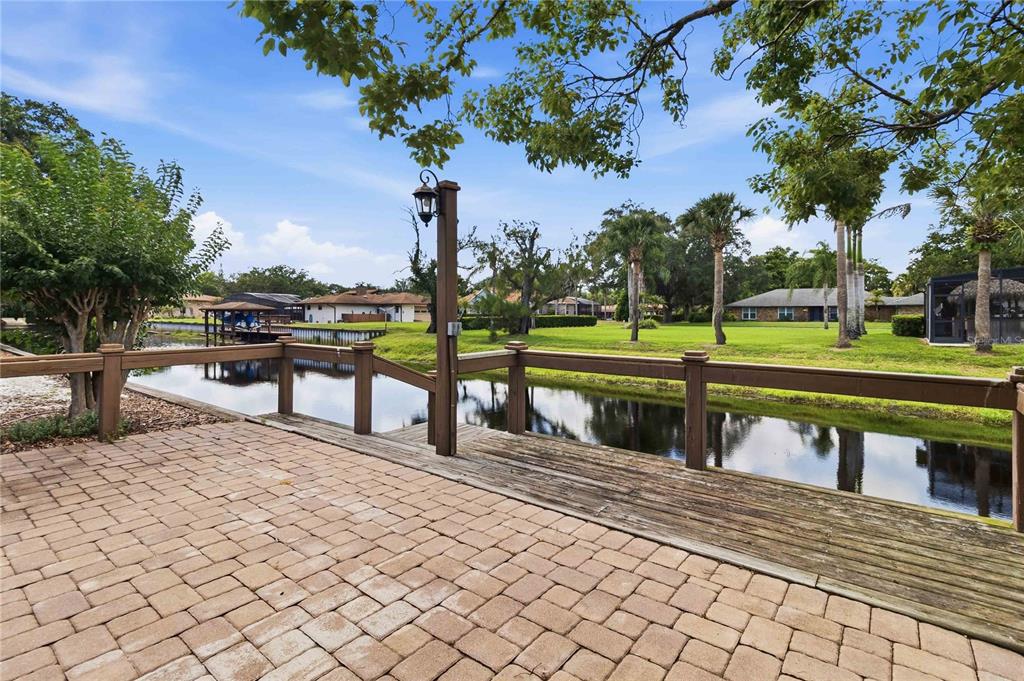 A paved patio overlooks a canal with a wooden deck and railing — 5367 CROOKED OAK CIRCLE, ST CLOUD, FL