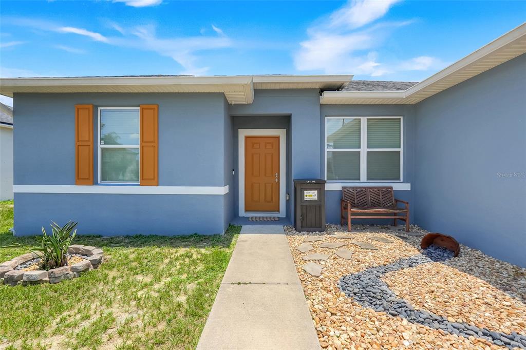 The exterior of a blue house features an orange front door, shutters, and a walkway — 1109 N PLATTE LANE, POINCIANA, FL
