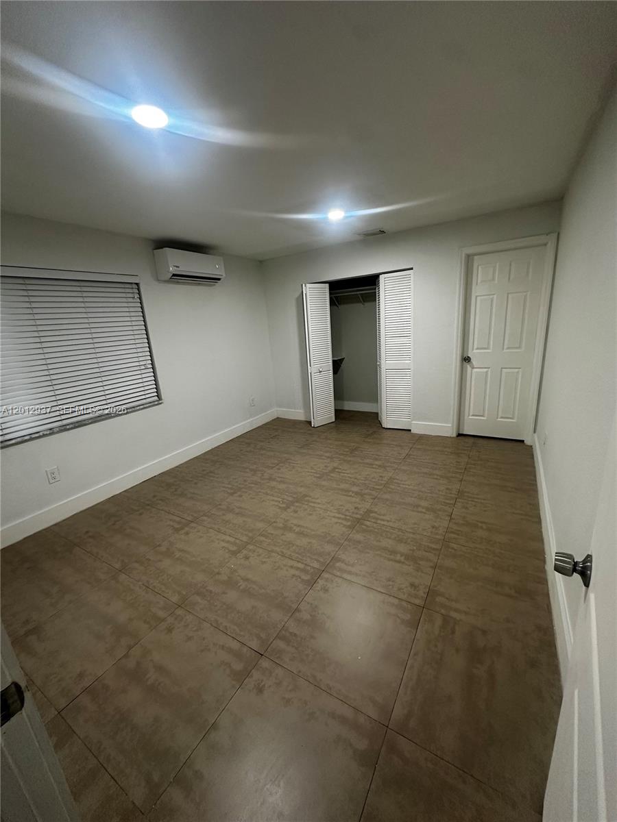 This bedroom features light-colored walls, large brown floor tiles, a closet, and a wall-mounted AC — 18560 SW 128th Ave # B, Miami FL 33177, MIAMI, FL