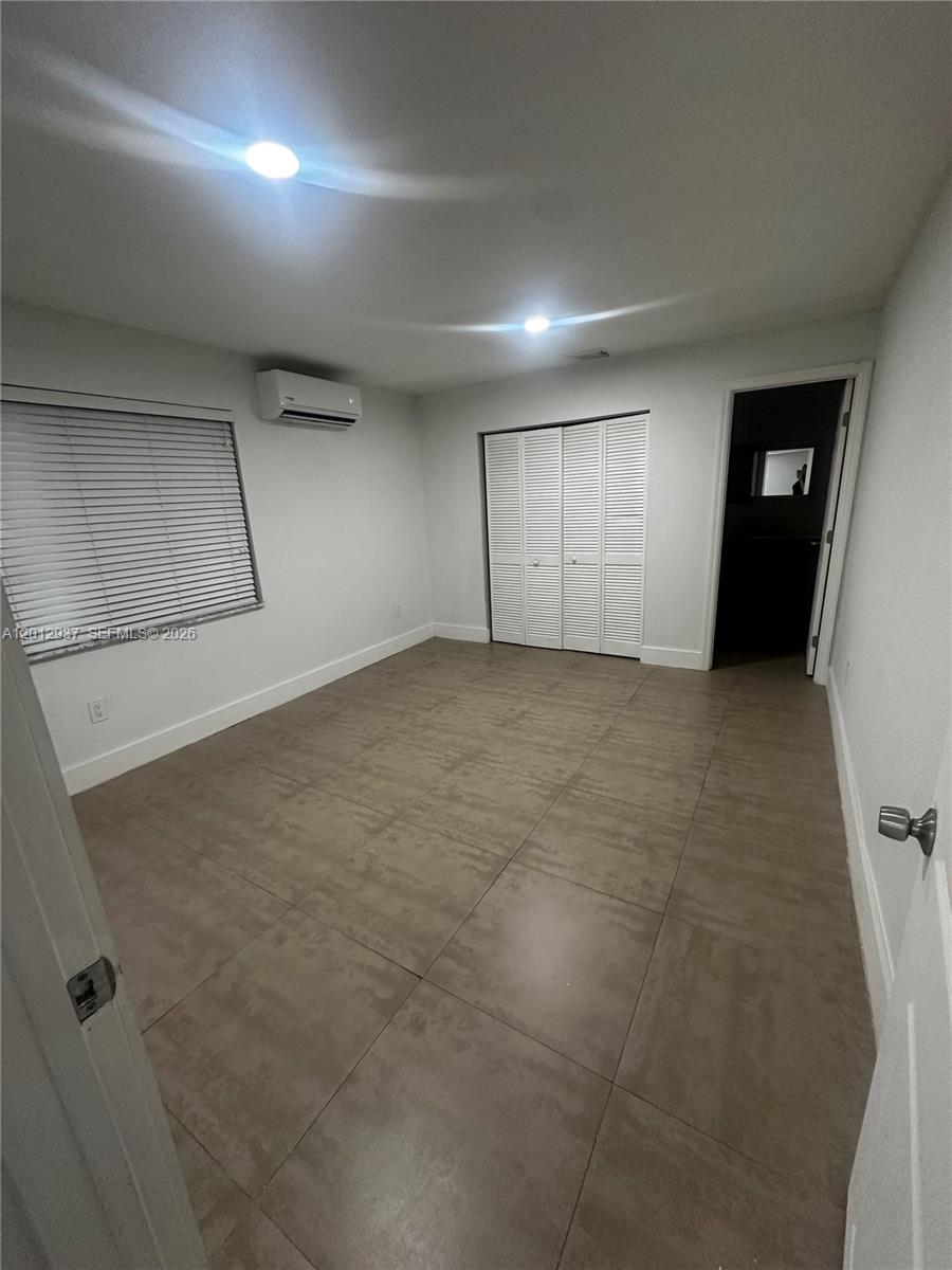 An empty bedroom features large beige floor tiles, white walls, a closet, and a mini-split unit — 18560 SW 128th Ave # B, Miami FL 33177, MIAMI, FL