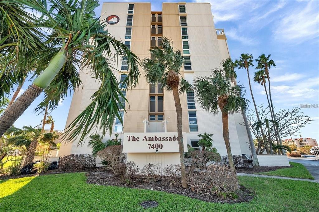 A low-angle view of the exterior of a multi-story beige apartment building with palm trees — 7400 SUN ISLAND DRIVE S UNIT 412, SOUTH PASADENA, FL
