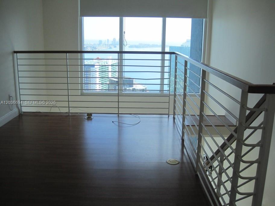 A loft area features dark wood flooring, a metal railing, and a large window overlooking water — 60 SW 13th St # 4610, Miami FL 33130, MIAMI, FL