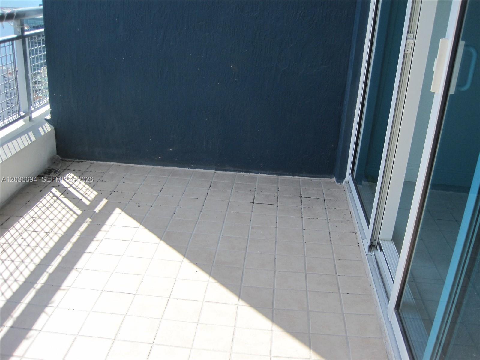 A balcony with light-colored square floor tiles, a dark blue wall, and a metal railing — 60 SW 13th St # 4610, Miami FL 33130, MIAMI, FL