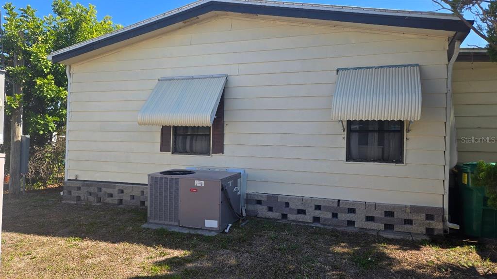 The exterior side of a light-colored house features two windows with awnings and an AC unit — 854 CALLE MENUDA, ENGLEWOOD, FL