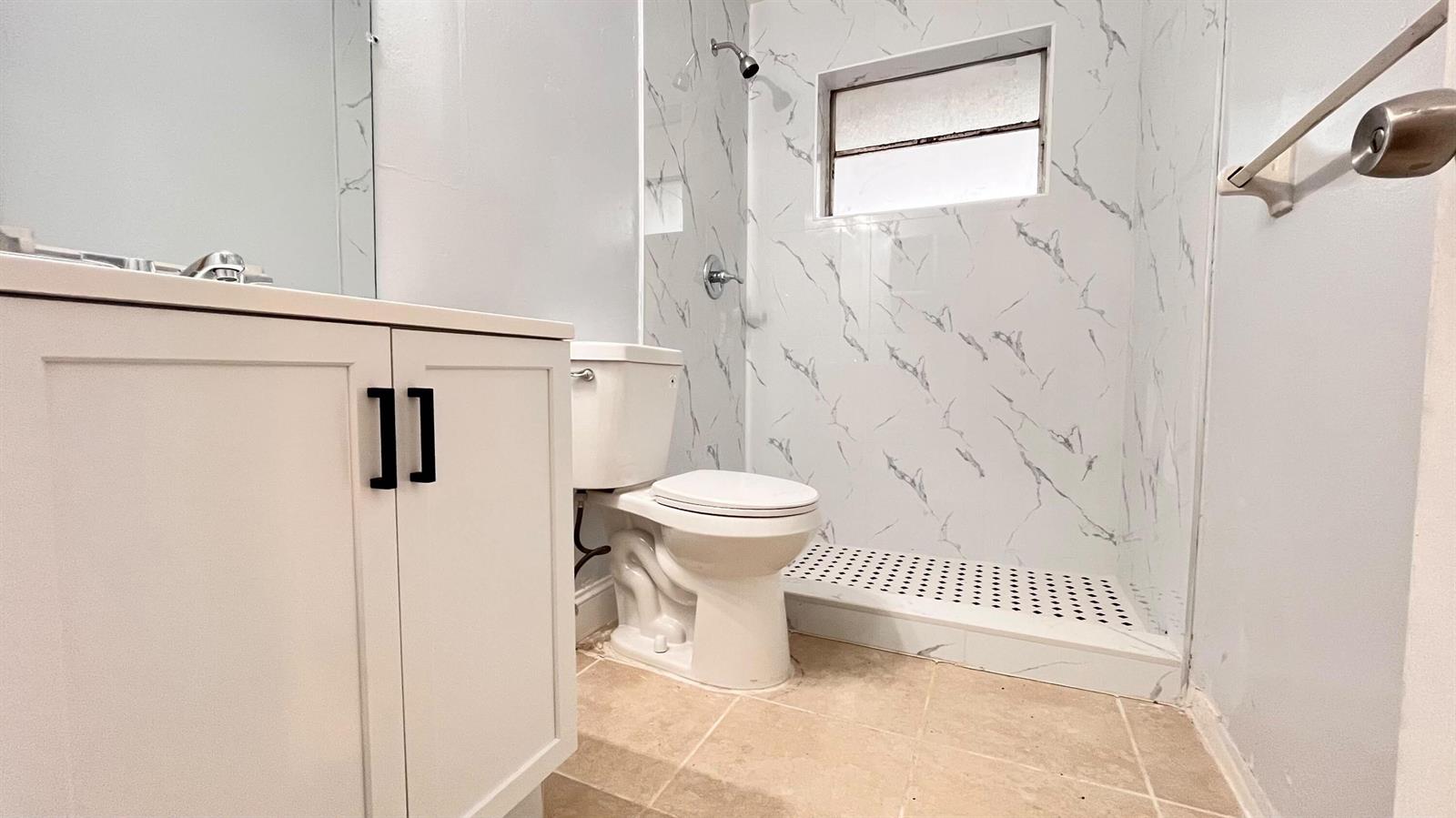 A bathroom features a white vanity, a toilet, and a walk-in shower with marble-patterned walls — 919 S G Street, FL 33460, FL