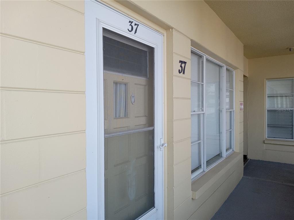 A light yellow exterior wall features a white screen door and window labeled 37 — 2459 FRANCISCAN DRIVE UNIT 37, CLEARWATER, FL