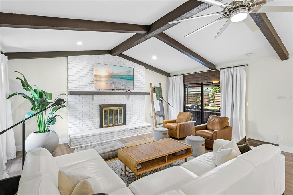 A living room features a white brick fireplace, vaulted ceilings with exposed beams, and white sofas — 6513 29TH AVENUE W, BRADENTON, FL