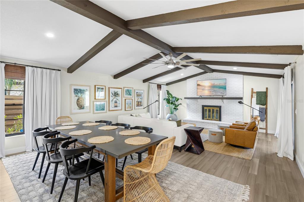 A dining and living area features vaulted ceilings with exposed beams and a brick fireplace — 6513 29TH AVENUE W, BRADENTON, FL