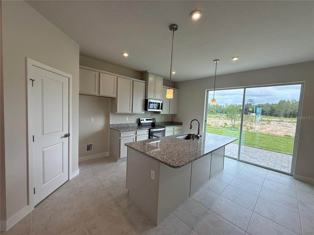 A kitchen features light-colored cabinets, granite countertops, a center island, and sliding glass doors — 1241 PINEYWOOD FIELD DRIVE, DAVENPORT, FL