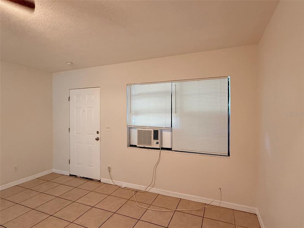 A room with beige tile flooring, a white door, and a window-mounted air conditioning unit — 2404 10TH STREET W UNIT 4, BRADENTON, FL