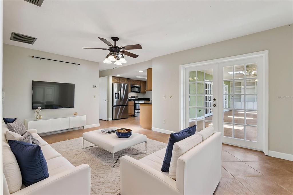 A living room with white sofas, a television, and French doors leading to a sunroom — 215 TWELVE LEAGUE CIRCLE, CASSELBERRY, FL