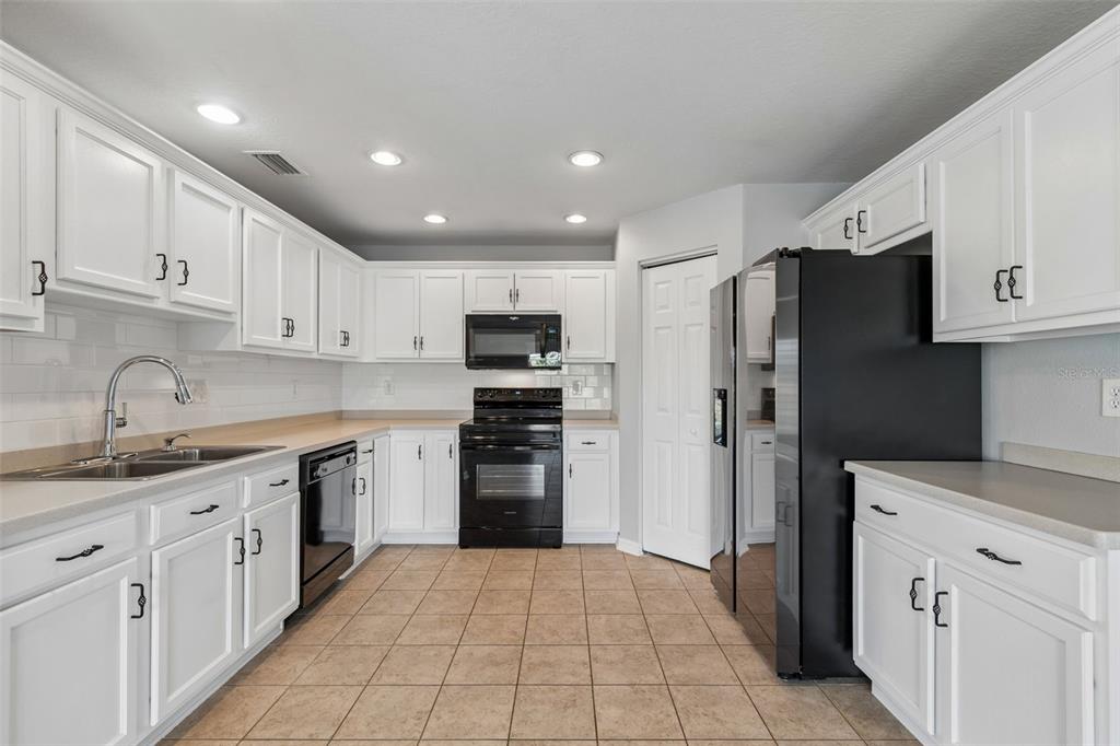 A kitchen with white cabinets, black appliances, light countertops, and tan tile flooring — 9515 SIMEON DRIVE, LAND O LAKES, FL