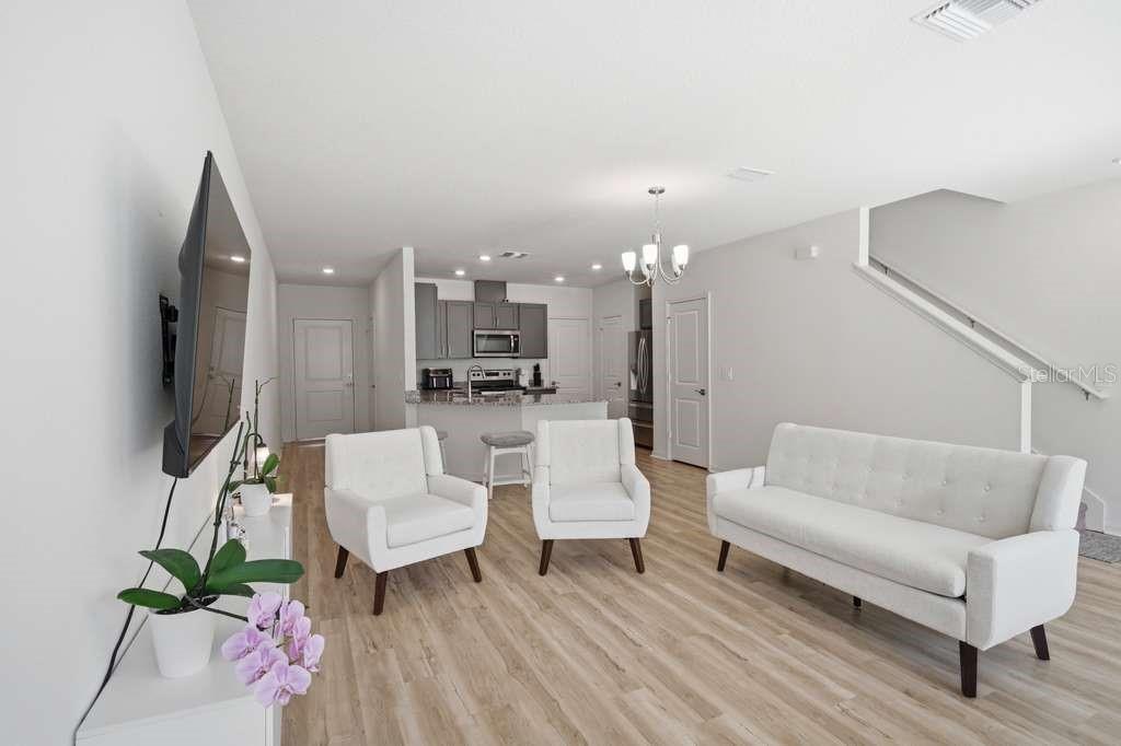 A living room with light wood floors, white furniture, and an open kitchen in the background — 9424 WESTSIDE HILLS DRIVE, DAVENPORT, FL