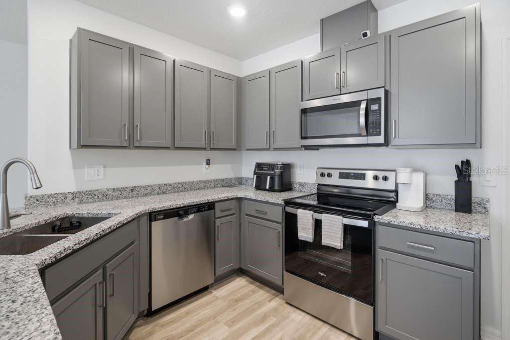 A kitchen features gray cabinets, granite countertops, and stainless steel appliances — 9424 WESTSIDE HILLS DRIVE, DAVENPORT, FL