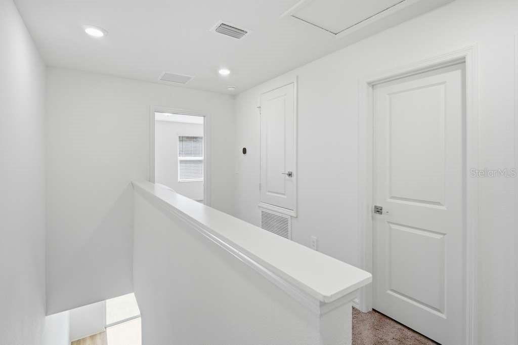 A white hallway features a staircase railing, a closed door, and a utility closet door — 9424 WESTSIDE HILLS DRIVE, DAVENPORT, FL
