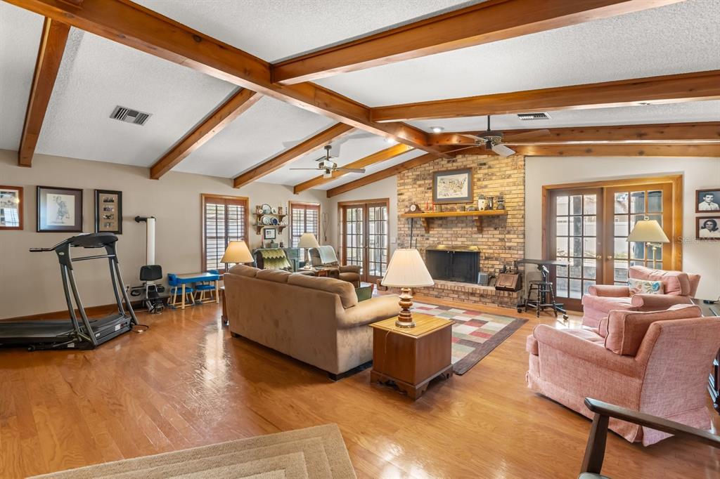 A living room features vaulted ceilings with exposed wood beams, a brick fireplace, and hardwood floors — 4925 HOPERITA STREET, ORLANDO, FL