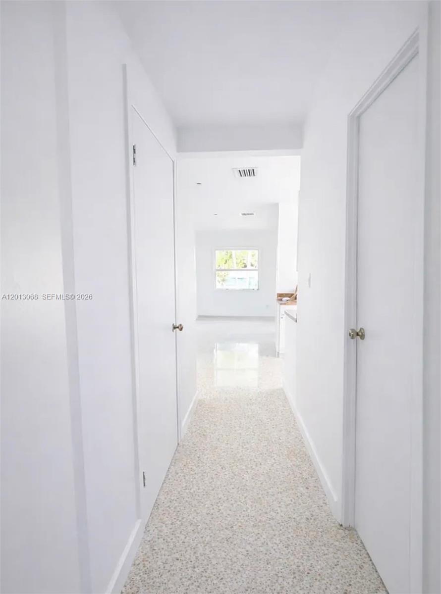 A narrow hallway with white walls and speckled terrazzo flooring leads toward a bright room — 34 SE 1st Ave # B, Dania Beach FL 33004, DANIA BEACH, FL