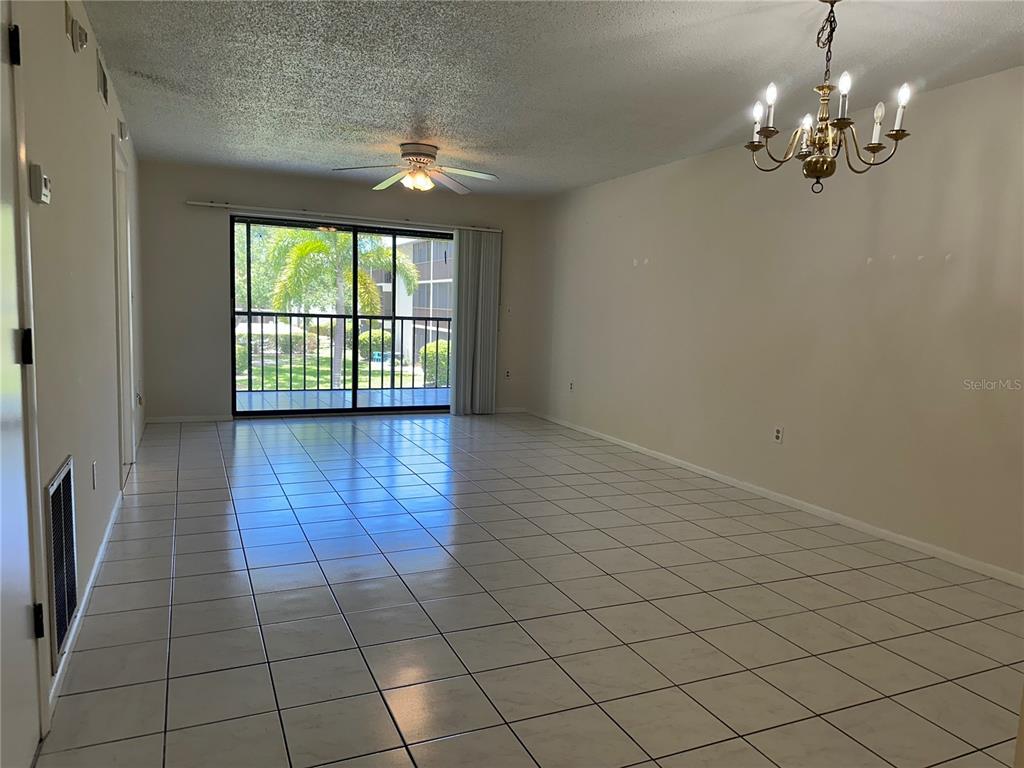 An empty living room features white tile floors, a ceiling fan, and a sliding glass door — 7205 CURTISS AVENUE UNIT 2B, SARASOTA, FL