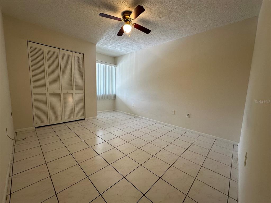 An empty room with white tile flooring, a ceiling fan, and white louvered closet doors — 7205 CURTISS AVENUE UNIT 2B, SARASOTA, FL