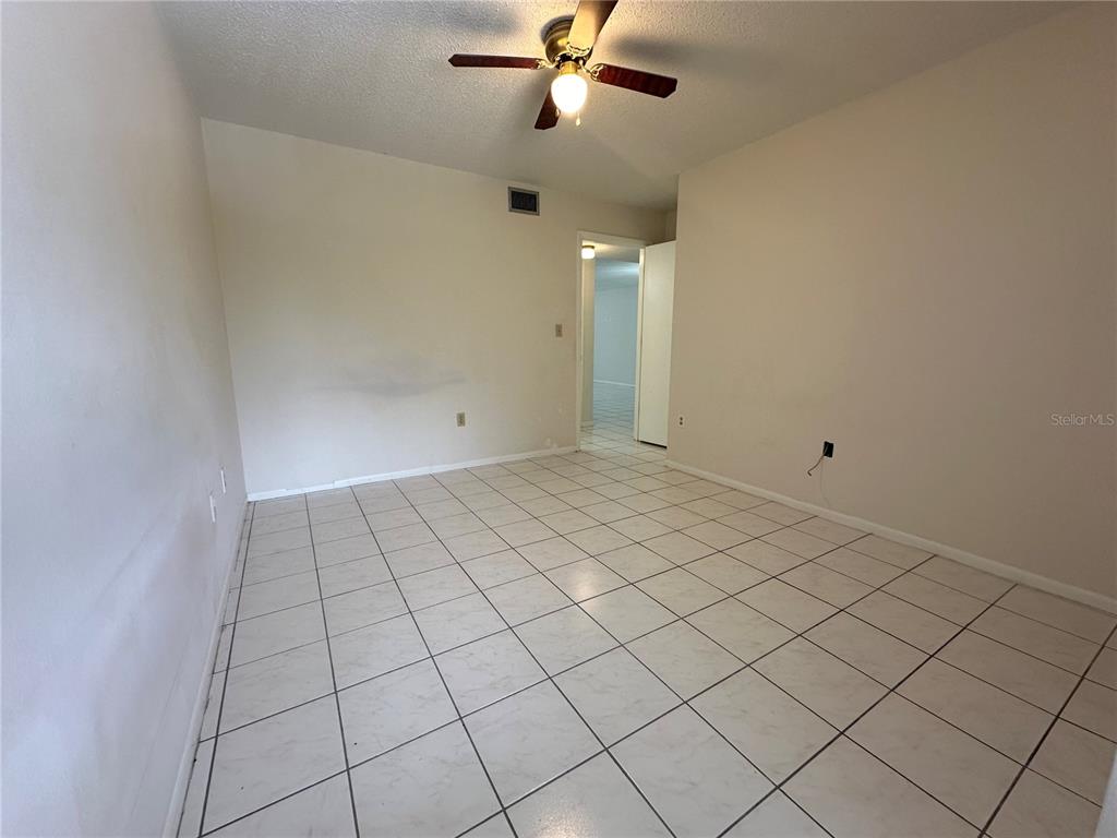 An empty room features white tile flooring, beige walls, and a ceiling fan — 7205 CURTISS AVENUE UNIT 2B, SARASOTA, FL
