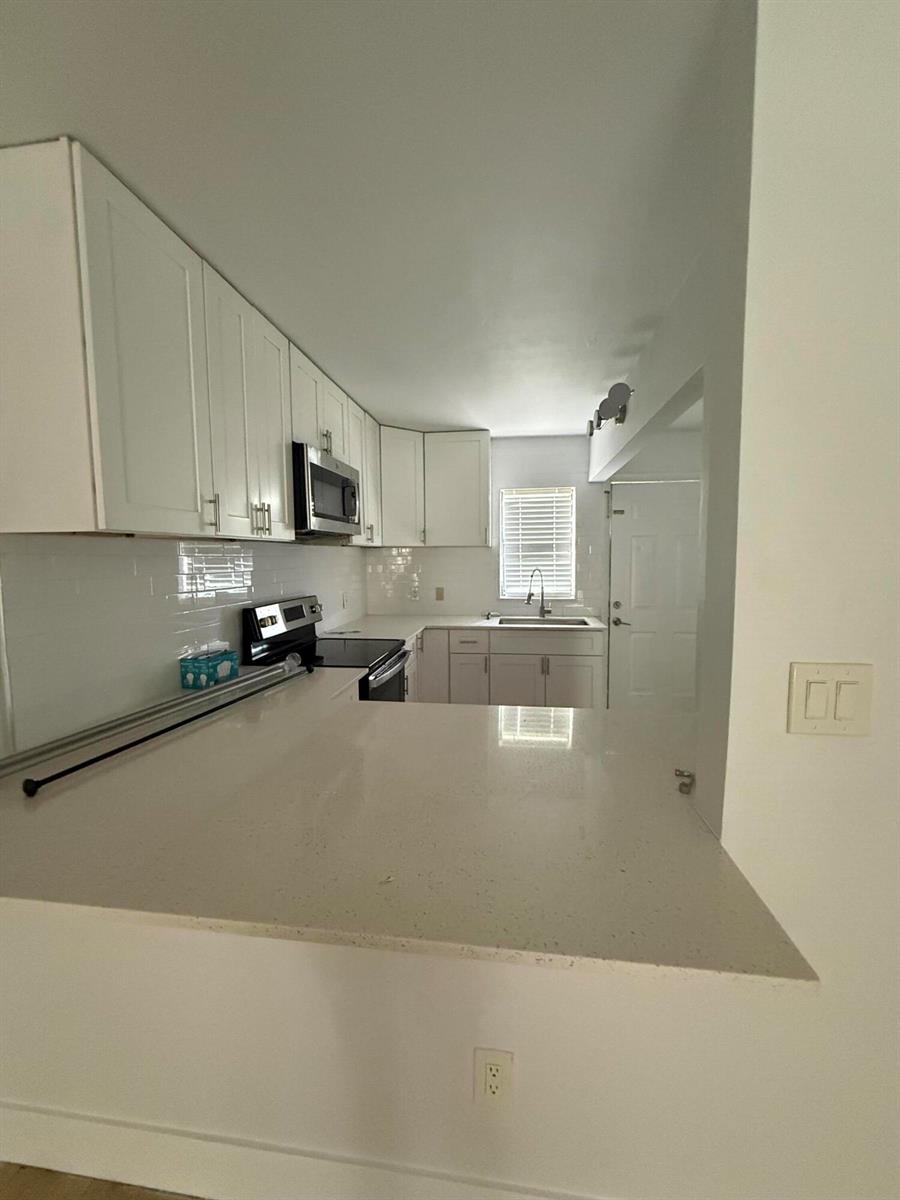 A kitchen features white cabinets, light countertops, a stainless steel microwave, and a subway tile backsplash — 605 Ixoria # 4, Fort Pierce FL 34982, FORT PIERCE, FL