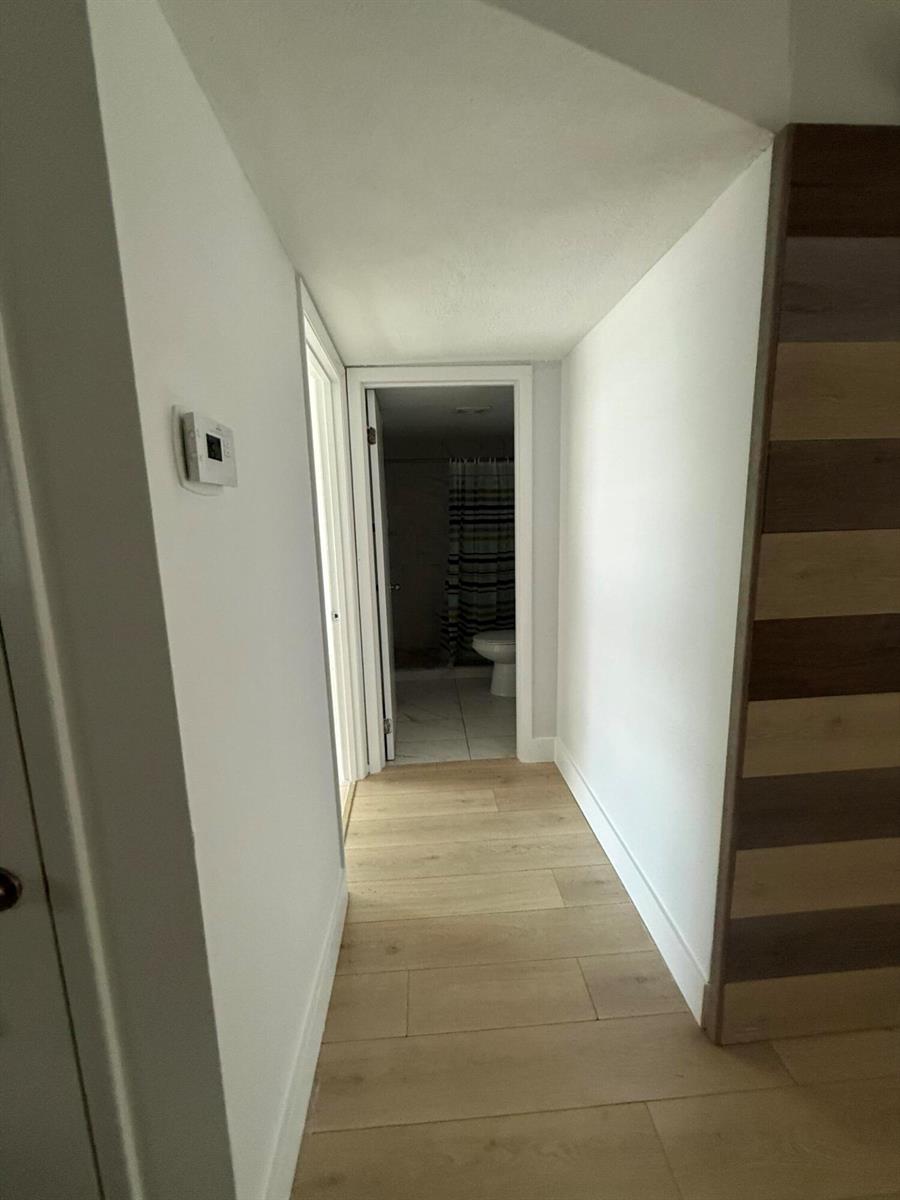 A hallway with light wood-look flooring leads to a bathroom with a shower curtain — 605 Ixoria # 4, Fort Pierce FL 34982, FORT PIERCE, FL