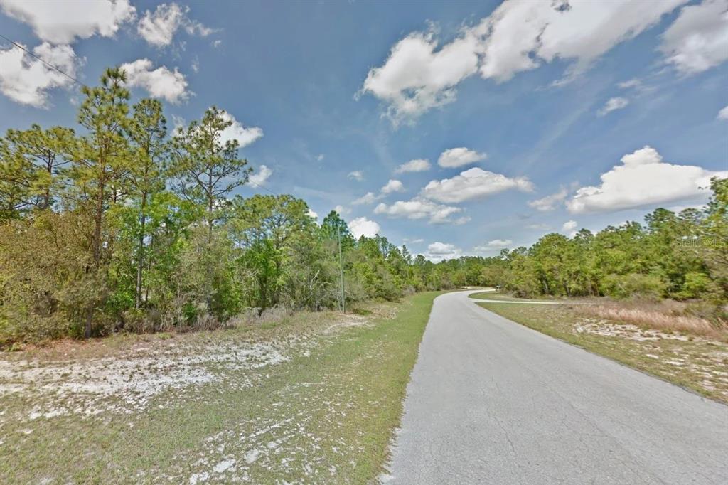A paved road winds through a wooded area with sandy ground and a blue sky — 000 MARION OAKS PASS, OCALA, FL
