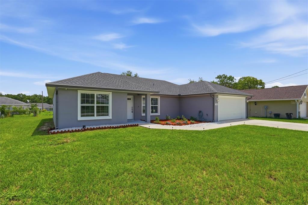 A single-story gray house with a white garage door and a green lawn — 15055 SE 93RD COURT, SUMMERFIELD, FL