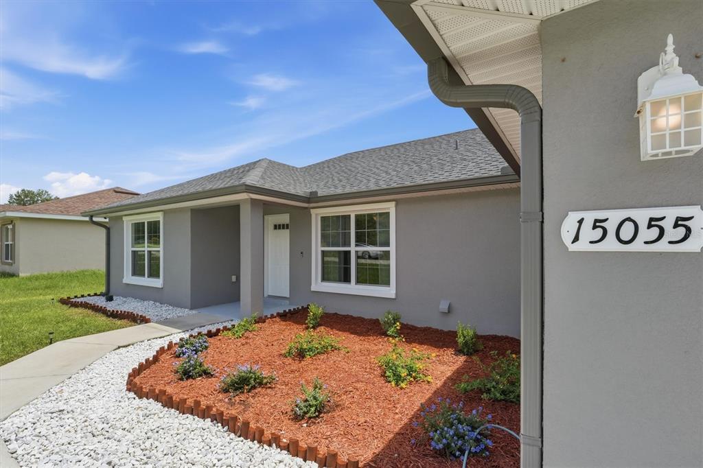 The exterior of a gray house features a white front door, windows, and landscaping — 15055 SE 93RD COURT, SUMMERFIELD, FL