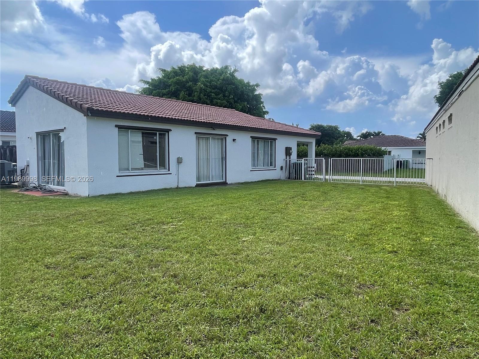 The exterior of a white house features a red tile roof and a grassy backyard — 14252 SW 175th Ter, Miami FL 33177, MIAMI, FL