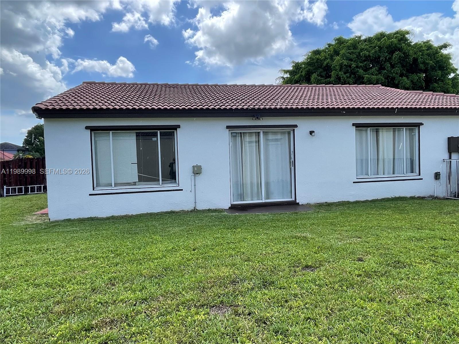 The exterior of a white, single-story house features a tiled roof and a grassy yard — 14252 SW 175th Ter, Miami FL 33177, MIAMI, FL