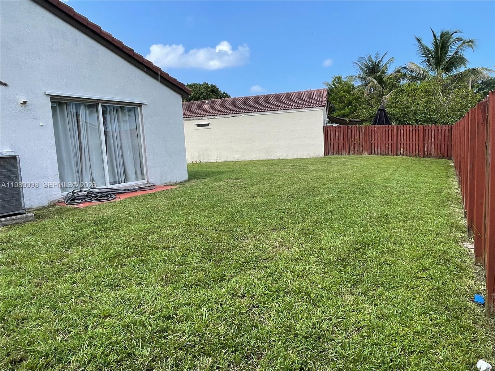 A backyard features a grassy lawn, a white house with sliding doors, and a wooden fence — 14252 SW 175th Ter, Miami FL 33177, MIAMI, FL