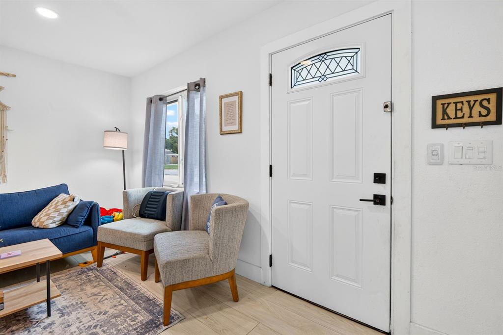A living room features a blue sofa, two armchairs, a white front door, and light flooring — 707 65TH AVENUE DRIVE W, BRADENTON, FL