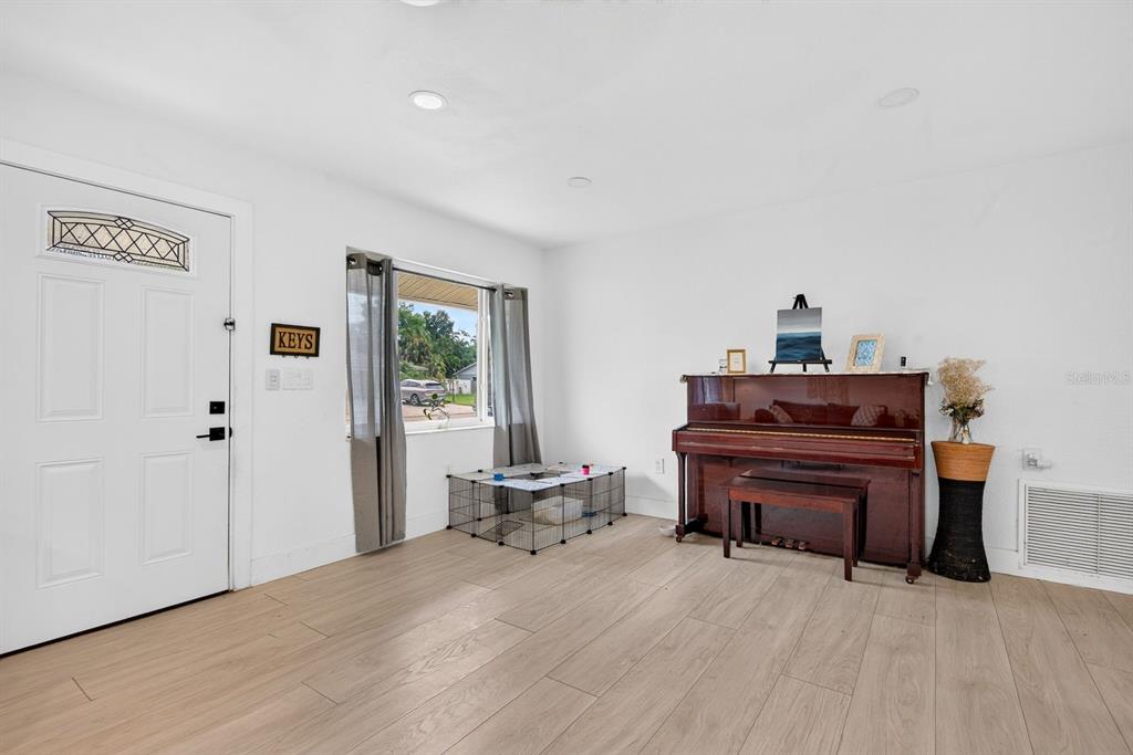 A living room features light wood-look flooring, a piano, a pet playpen, and a front door — 707 65TH AVENUE DRIVE W, BRADENTON, FL